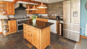 A kitchen with wooden cabinets, a central island, stainless steel appliances, and a stone backsplash. - Apple Barn (South Molton)
