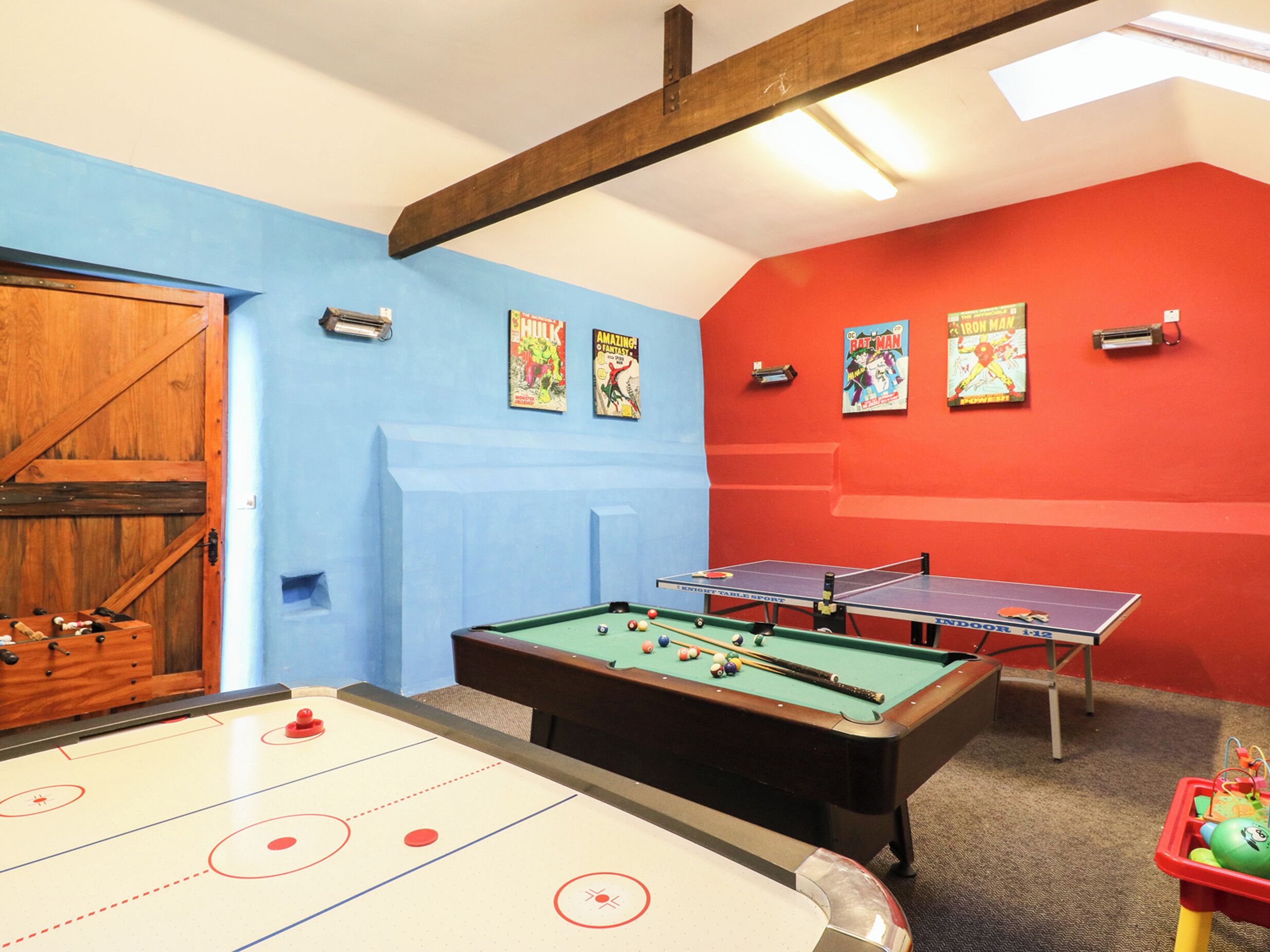 A room with a pool table, two ping pong tables, and a shuffleboard table.