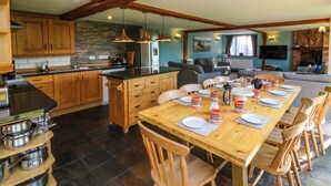 A spacious kitchen with wooden cabinets, a dining area with a wooden table set for four, and a living area with a sofa and a television. - Apple Barn (South Molton)