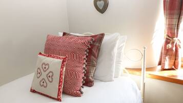 Un dormitorio con cama, almohadas, un adorno con forma de corazón en la pared y una ventana con cortinas.