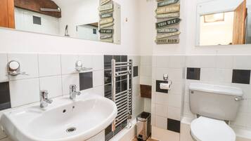 A modern bathroom with a white sink, a toilet, and a towel rack. There are black and white tiles on the walls and a skylight above the sink.