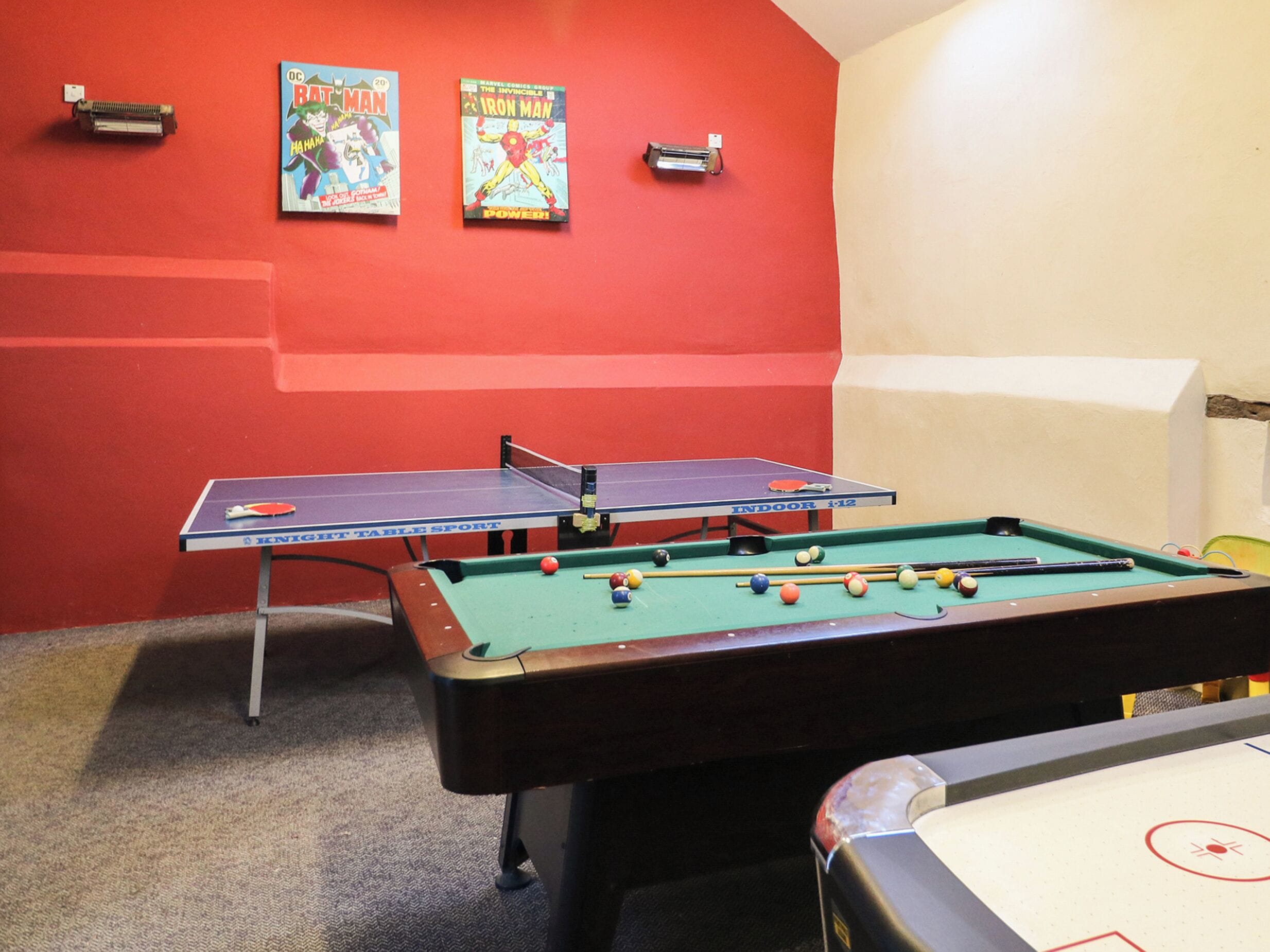 A room with a pool table, a ping pong table, and two posters on the wall.