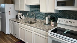 A kitchen with white cabinets, a granite countertop, a stainless steel sink, a microwave, and a stove.