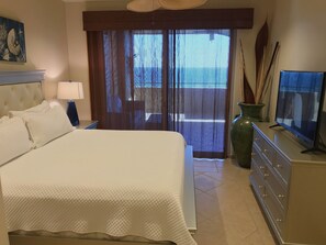 A hotel room with a large bed, a TV on a dresser, a large vase, and a view of the outdoors.