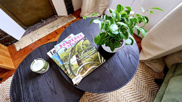 Una mesa redonda con una revista, una vela y una planta en maceta.