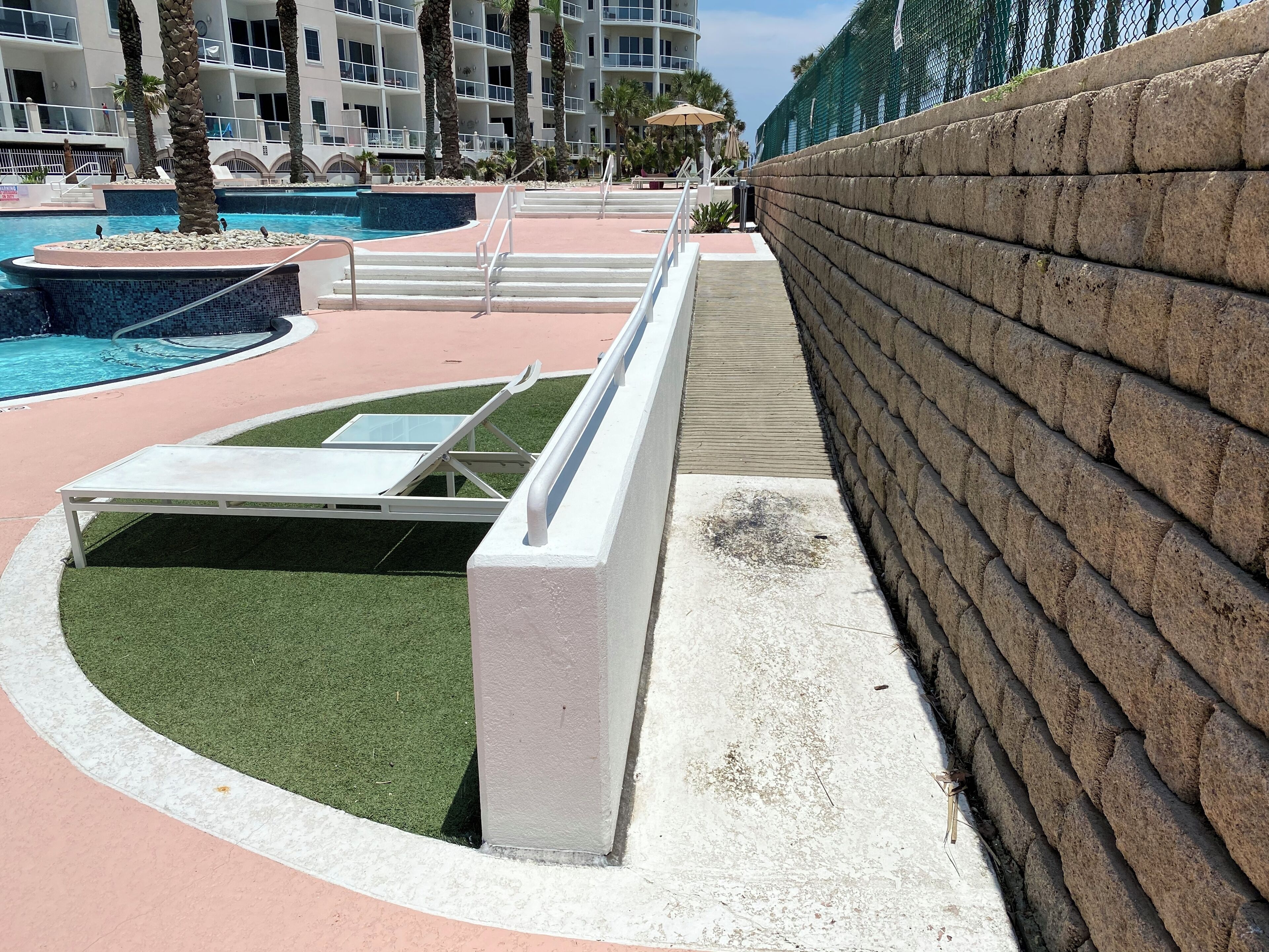 Un área de piscina con una tumbona, un muro de piedra y un edificio al fondo.
