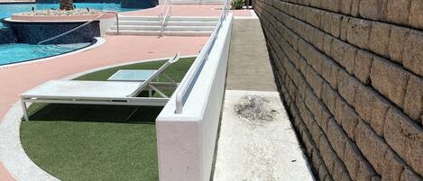 Un área de piscina con una tumbona, un muro de piedra y un edificio al fondo.