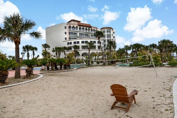 Une plage avec une chaise en bois, des palmiers et un grand bâtiment doté de nombreux balcons.