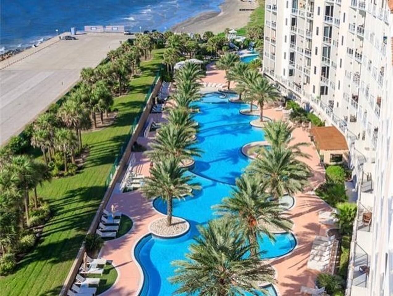 Un resort con piscina rodeada de palmeras y una playa.