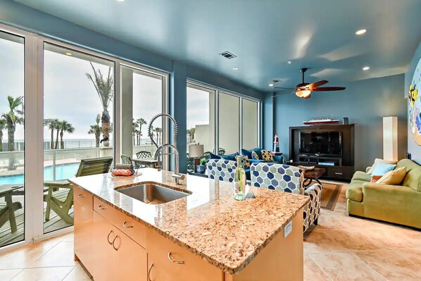 Una cocina moderna con una isla grande, un comedor con vistas a la piscina y una sala de estar con televisor y asientos.