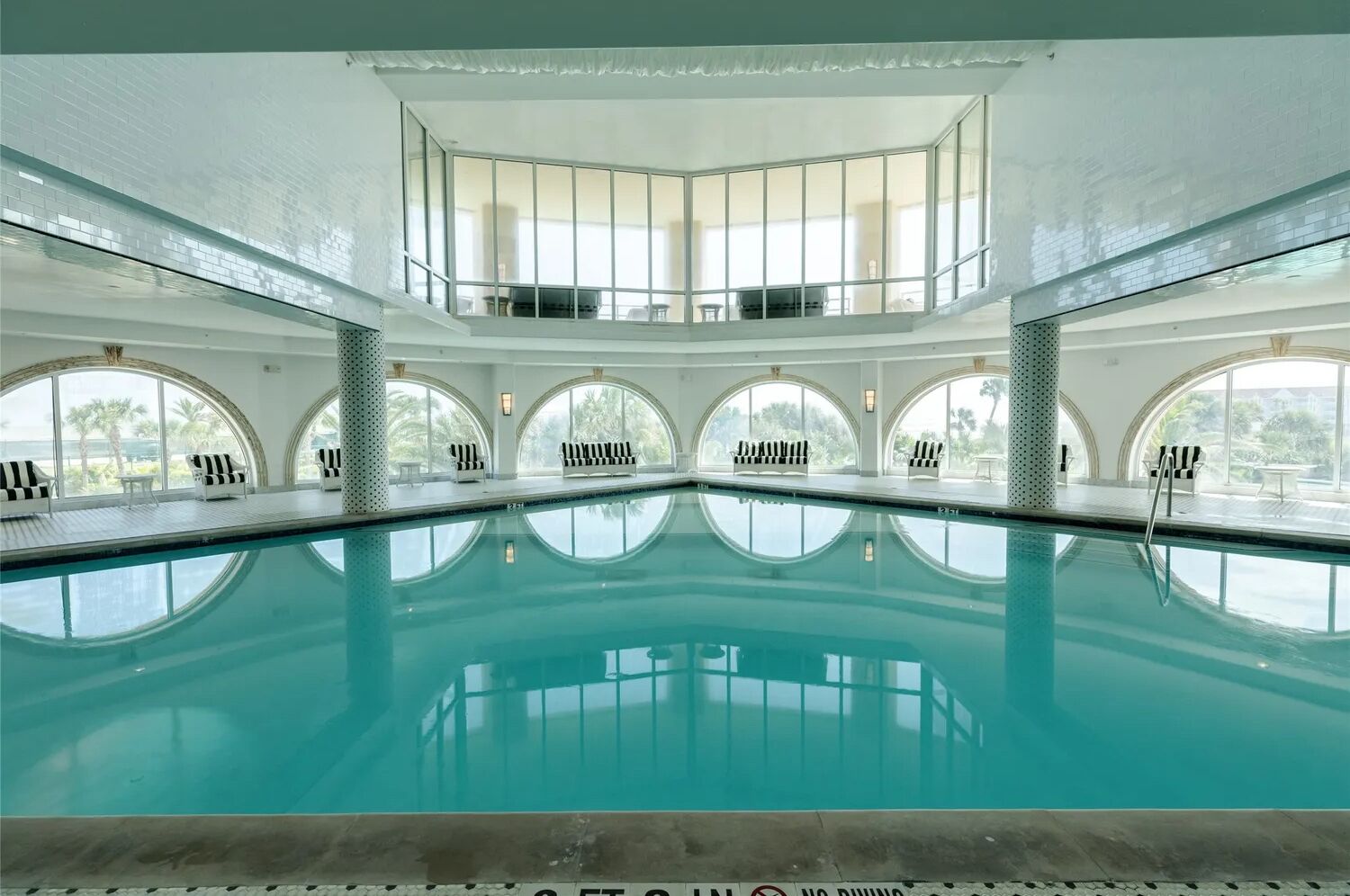 Una amplia piscina interior con varias zonas de descanso y grandes ventanales.