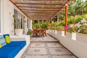 A covered outdoor seating area with a table and chairs, surrounded by potted plants and flowers.