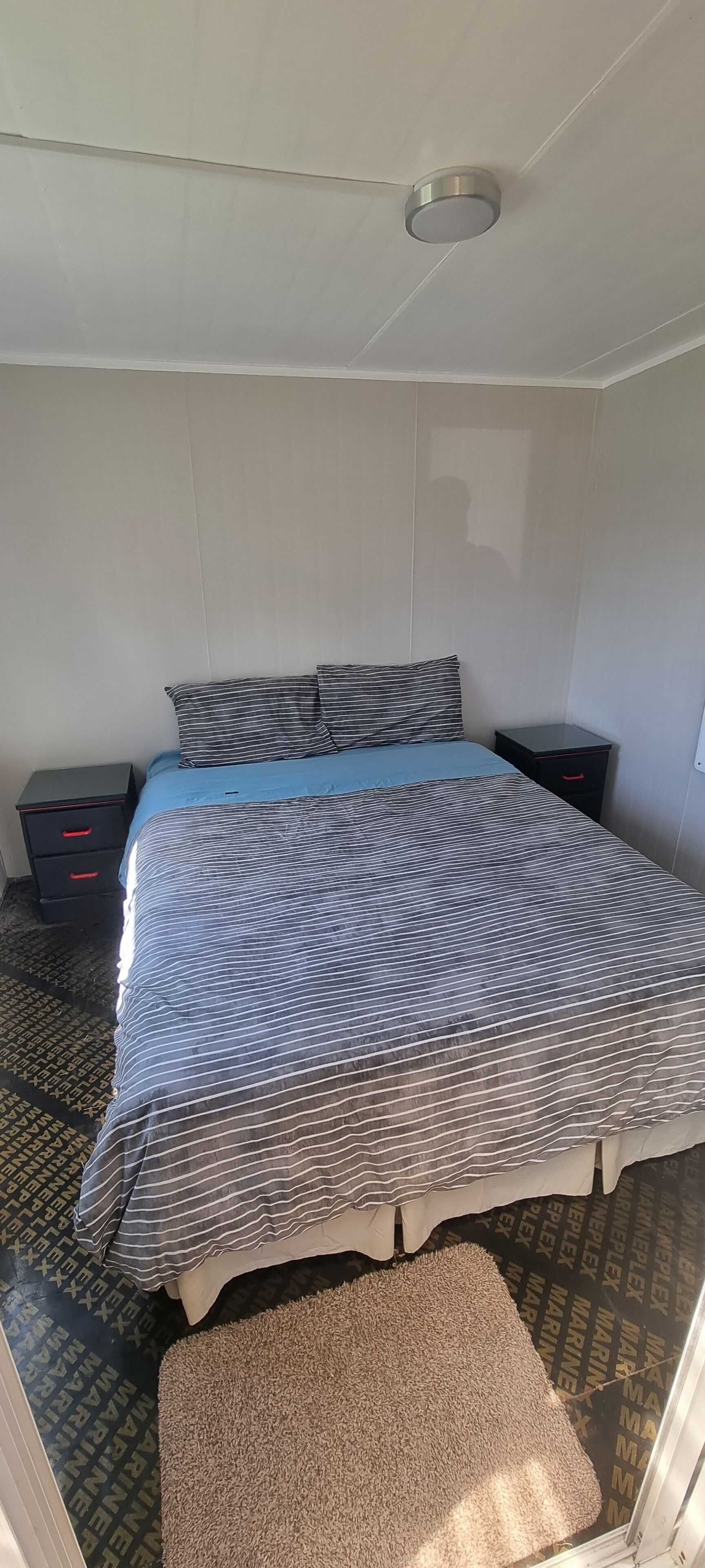 A bedroom with a bed, two nightstands, a ceiling light, and a patterned rug.