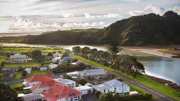 A coastal town with a prominent red-roofed building, a river, and lush green hills in the background.