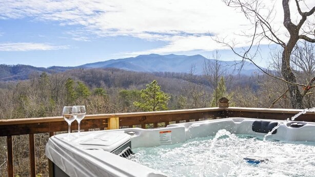 A hot tub with two glasses of wine on a wooden deck, overlooking a mountainous landscape. - Great View, Location, Studio Log Cabin, Hot Tub! (Gatlinburg)