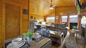 A wooden cabin interior with a dining area, a sofa, a fireplace, and a view of the mountains. - Great View, Location, Studio Log Cabin, Hot Tub! (Gatlinburg)