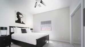 Un dormitorio con cama, una mesita de noche, un cuadro en la pared, una ventana con persianas y un ventilador de techo.