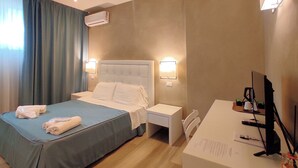 Habitación de hotel con cama, mesitas de noche, escritorio con computadora y unidad de aire acondicionado.