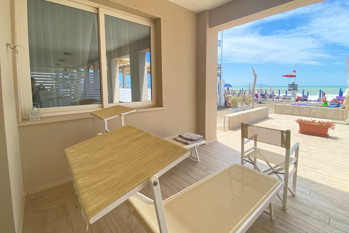 A balcony with a table and chairs, a view of the beach, and a potted plant.