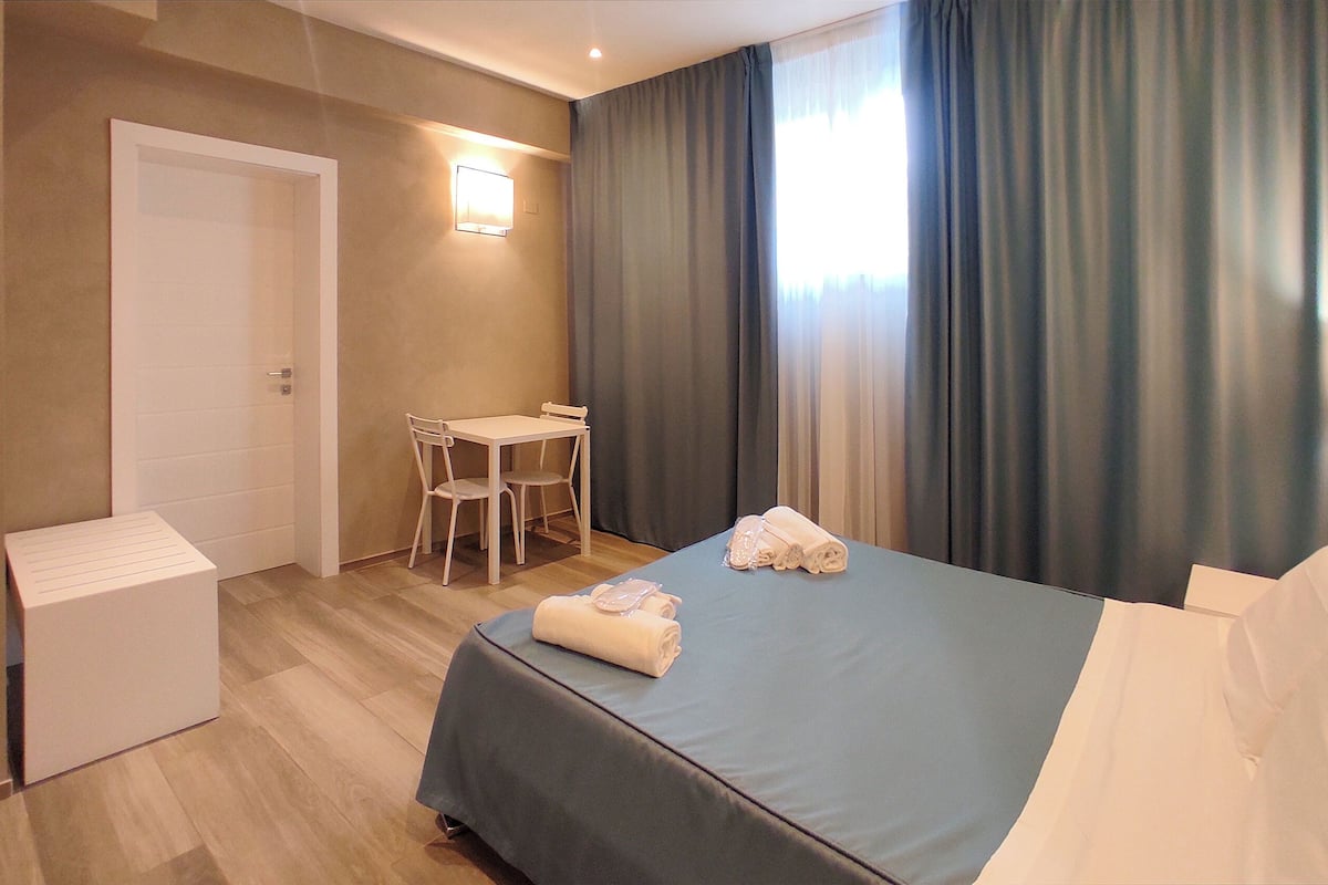 A hotel room with a bed, a desk, a chair, and a small white cabinet.
