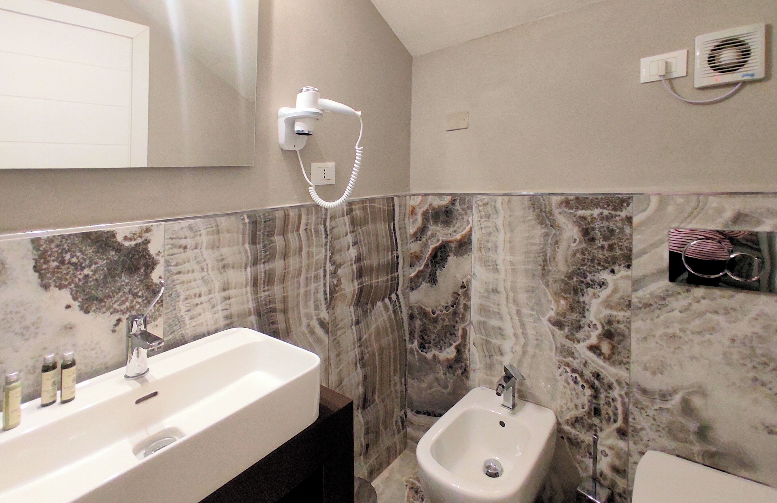 Een badkamer met een wastafel, een bidet en een aan de muur bevestigde haardroger.