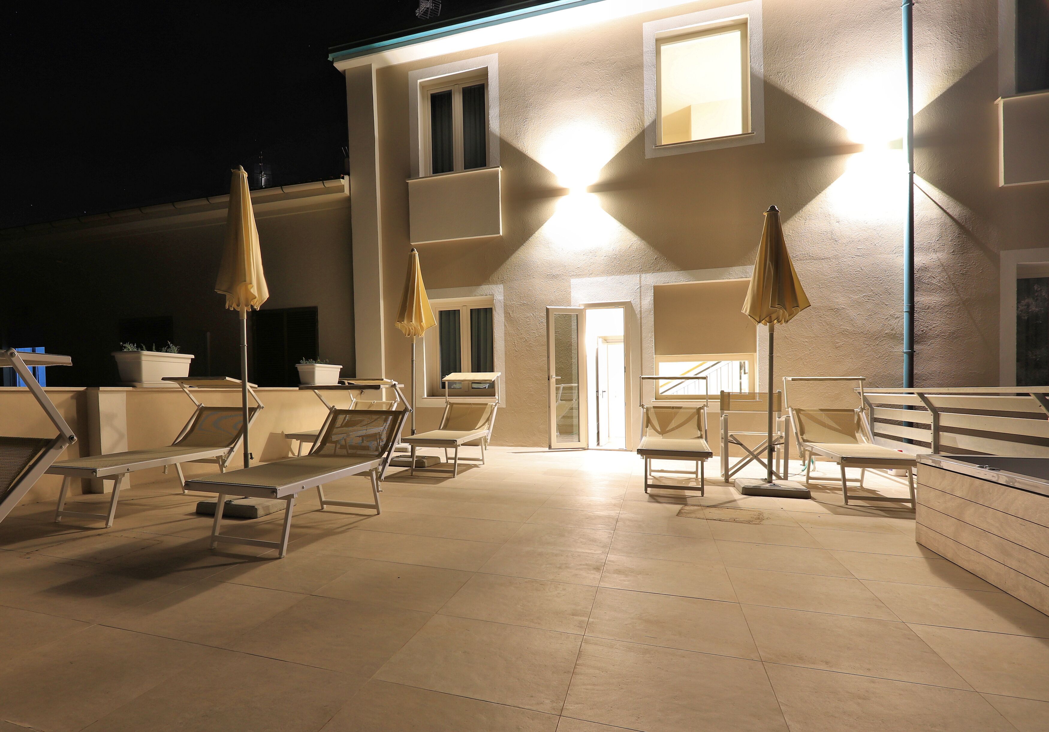 An outdoor seating area with lounge chairs and umbrellas, a building entrance, and a tiled patio.