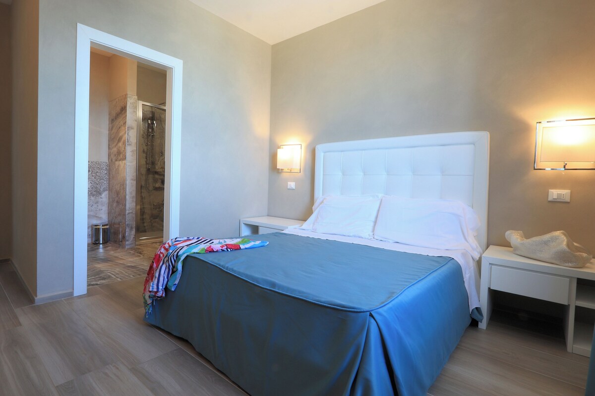 A hotel room with a bed, a nightstand, a wall-mounted light, and a shower area.