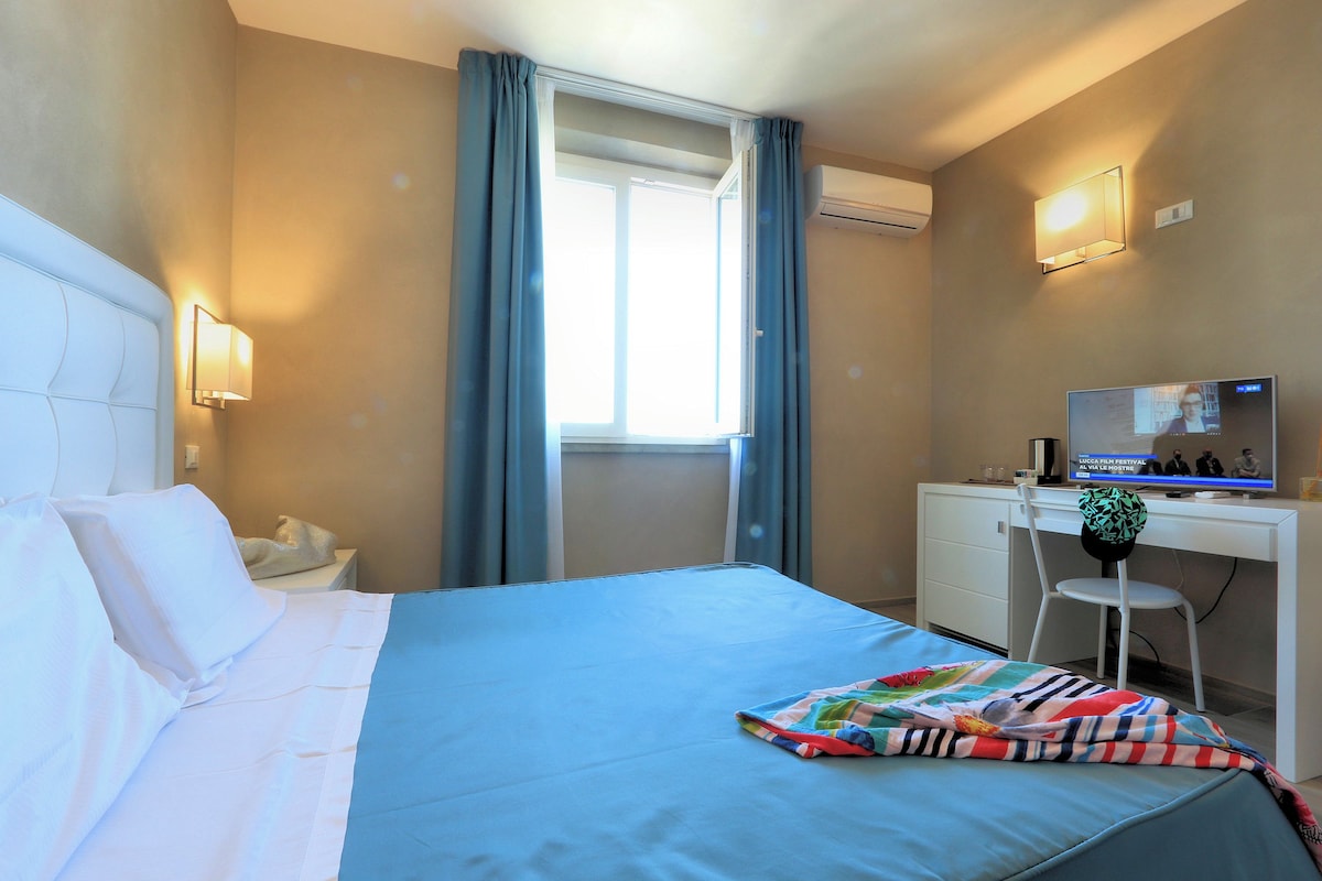 A hotel room with a bed, a desk, a chair, a TV, and a window with curtains.