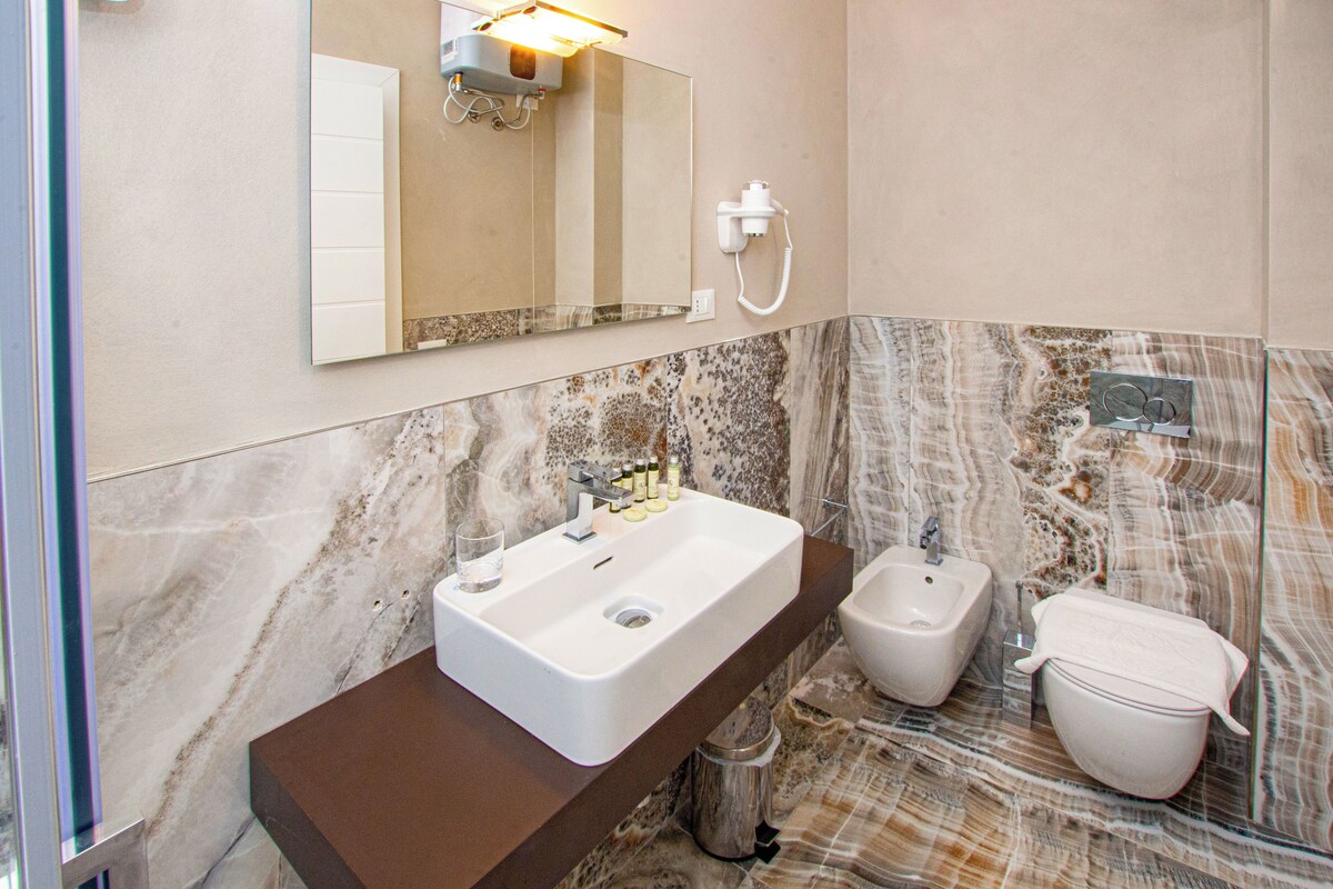 Un baño con lavamanos, bidé e inodoro de mármol, un espejo y un perchero para toallas.