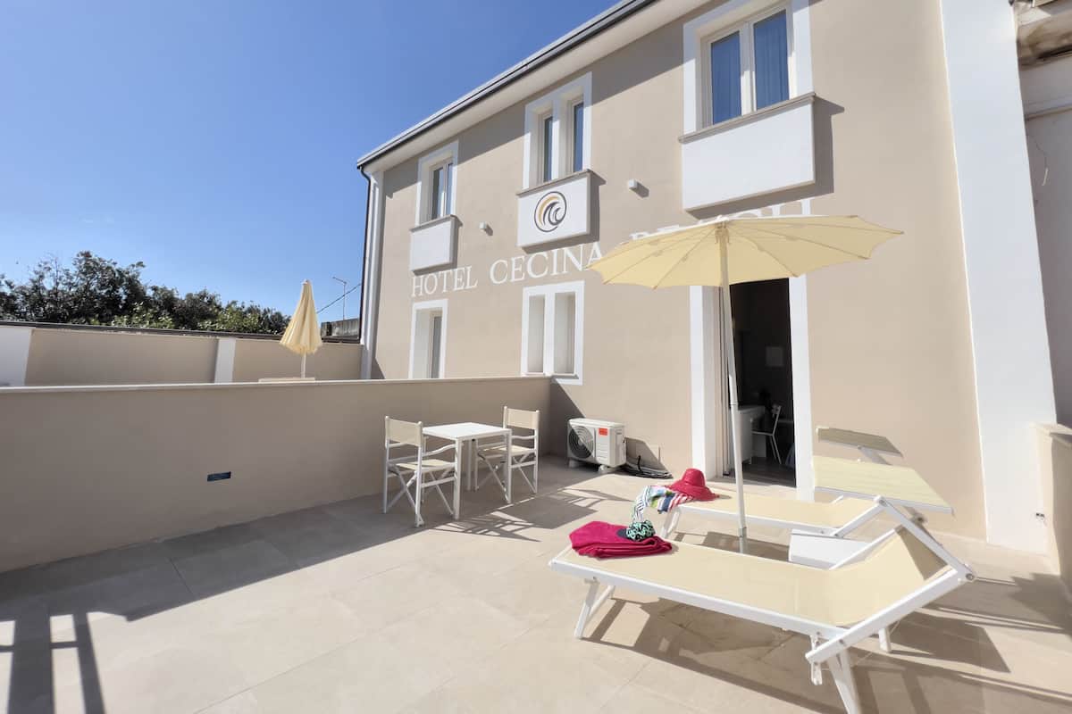 A hotel with a terrace featuring sun loungers, a table, and an umbrella.