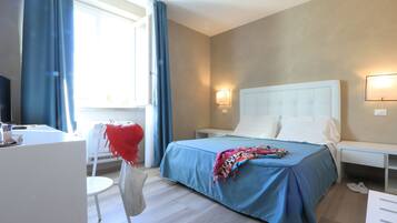 Habitación de hotel con cama, mesitas de noche, una silla, un escritorio y ventana con cortinas.