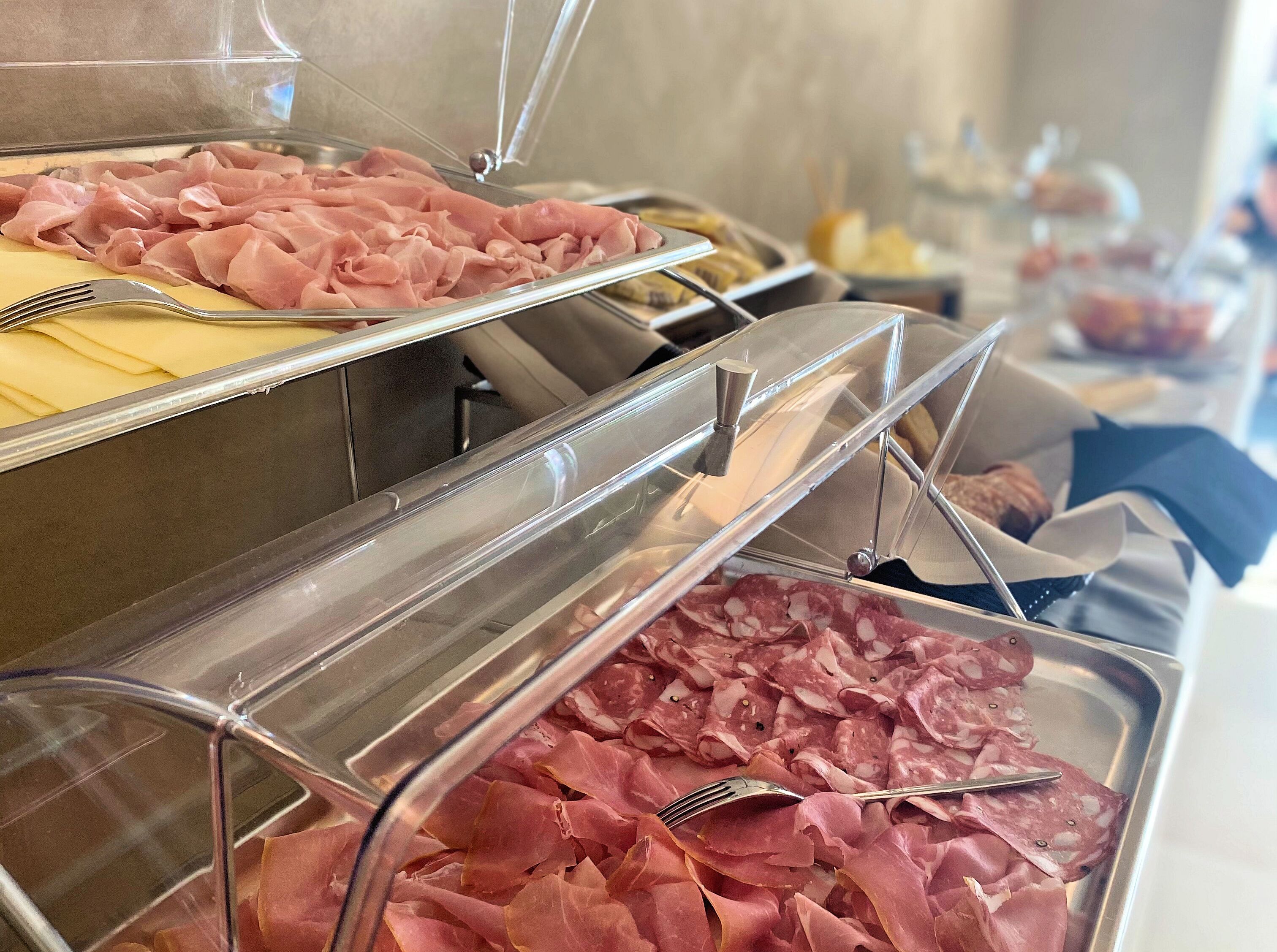 Buffet com diversos tipos de frios expostos em recipientes transparentes.