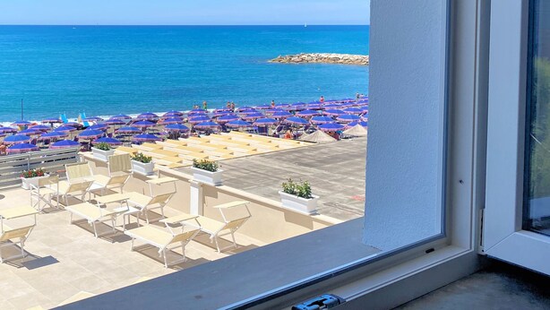 Vista de una playa con numerosas sombrillas y sillas de playa, un cielo azul despejado y el mar al fondo.