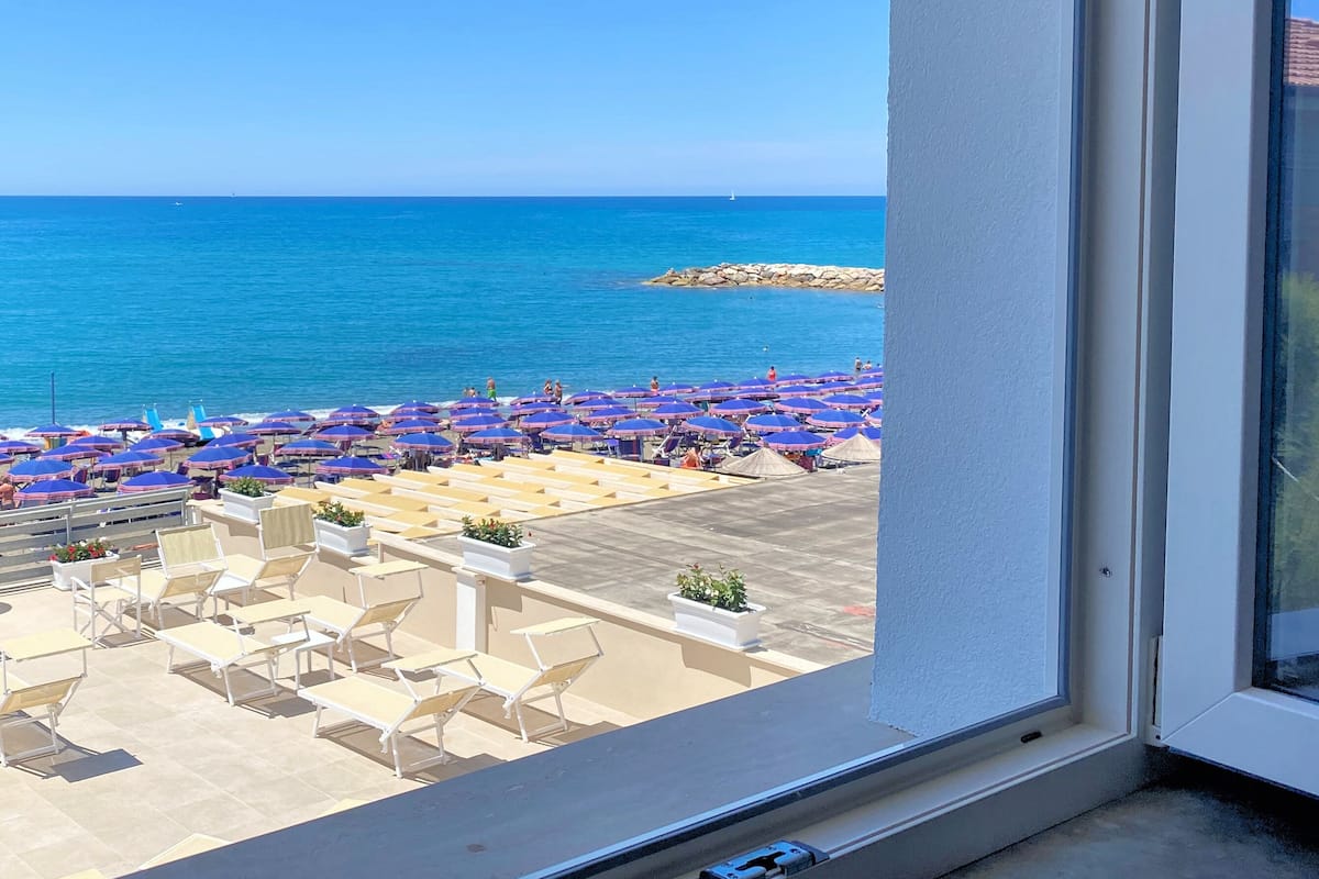 A view of a beach with numerous umbrellas and sun loungers, a clear blue sky, and the sea in the background.