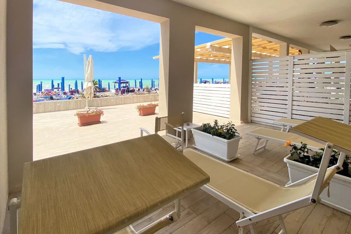 A beachside patio with outdoor seating, potted plants, and a view of the beach.