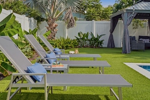 Un patio trasero con piscina, sillas de descanso y una pérgola.