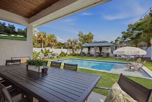 A poolside area with a table and chairs, a covered seating area, and a view of a golf course.