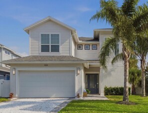 A two-story house with a garage, a front door, and a small porch with a bench.