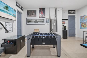 Una habitación con una mesa de futbolín, una mesa de futbolín con una pelota roja, una con una azul, una blanca, una negra, una amarilla y una verde, repitiéndose.