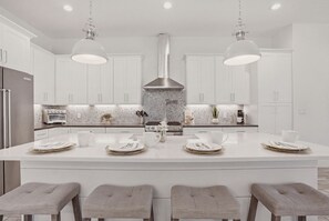 A modern kitchen with white cabinetry, a central island with bar stools, and pendant lighting.