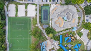 Eine Luftaufnahme eines Sportkomplexes mit mehreren Tennisplätzen, einem Spielplatz und Parkflächen.
