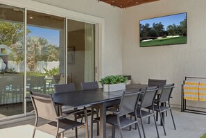An outdoor patio with a table and chairs, a sliding glass door leading to a pool, and a mounted television displaying a golf course. - Heated Pool | Golf Cart Perk | Close to the Beach (Jacksonville Beach)