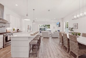 A modern kitchen with a central island, bar stools, and a dining area with wicker chairs. - Heated Pool, Golf Cart & Close to the Beach (Jacksonville Beach)