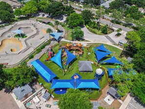 An aerial view of a park with a playground, a large blue tent-like structure, and a winding road.