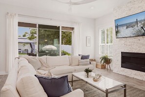 A modern living room with a white sofa, a glass coffee table, and a fireplace. - Heated Pool | Golf Cart Perk | Close to the Beach (Jacksonville Beach)