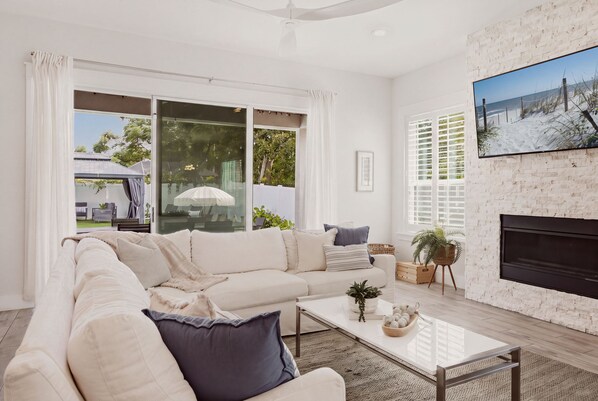 A modern living room with a white sofa, a glass coffee table, and a fireplace.