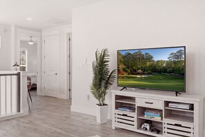 A modern living room with a flat-screen TV mounted on a wall, a potted plant, and a wooden entertainment unit with games and books.