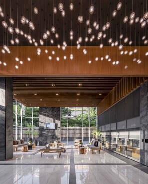 A spacious lobby with a high ceiling, hanging pendant lights, a central seating area, and large windows offering views of greenery. - Wyndham Garden Bangkok Sukhumvit 42 (Bangkok)