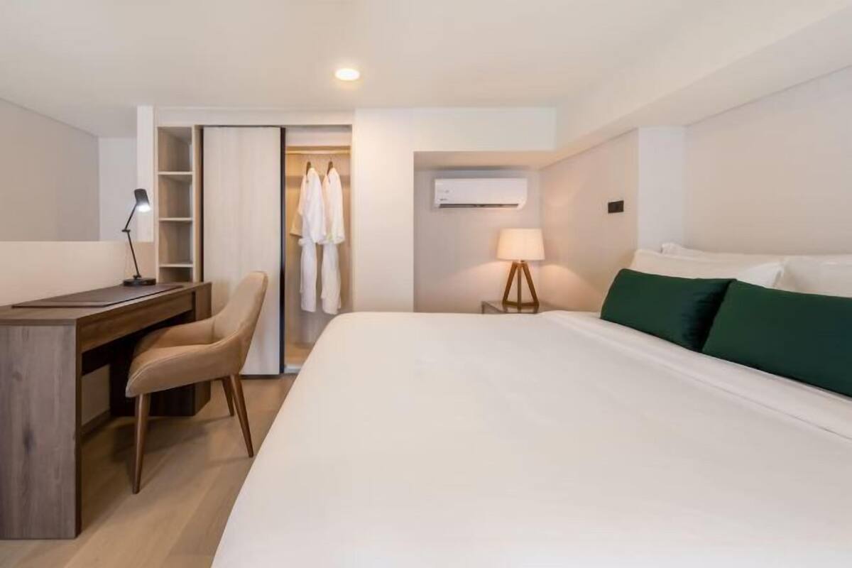 A hotel room with a bed, a desk, a chair, a wardrobe, and a lamp.