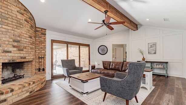 Un salon avec une cheminée en briques, un ventilateur de plafond, une horloge et une grande fenêtre.
